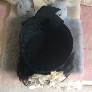 May include: A black straw hat with a black ribbon and white flower embellishments.