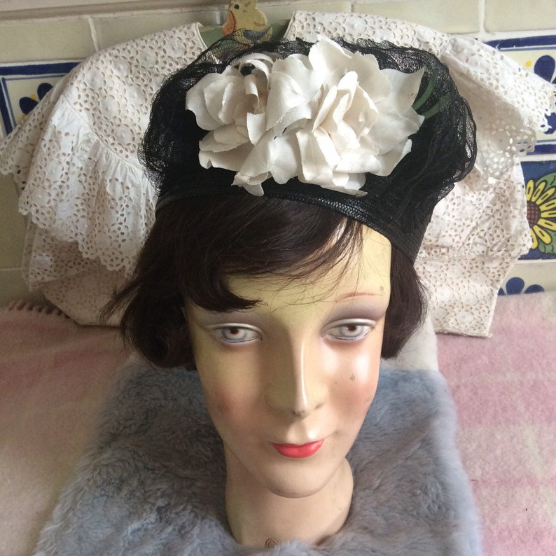 May include: A black and white hat with a large white flower on top. The hat is made of a fine mesh material and is sitting on a mannequin's head.
