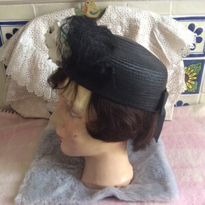 May include: A black straw hat with a black feather and net trim. The hat is on a mannequin head.