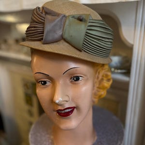 Könnte beinhalten: Ein Vintage-Hut mit braunem Strohhut und einer grünen und braunen Stoffschleife. Der Hut sitzt auf einem Mannequin-Kopf.