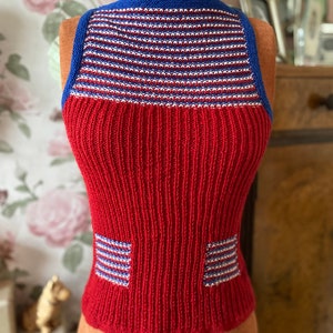 Peut inclure: Un haut en tricot rouge sans manches avec un col rayé bleu, blanc et rouge et deux petits panneaux rayés bleu, blanc et rouge sur le devant.