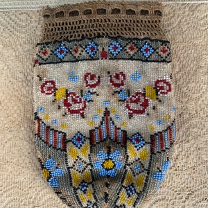 Può includere: Una borsa vintage di perline con una parte superiore all'uncinetto. La borsa è decorata con un motivo floreale in tonalità di rosso, blu e giallo.