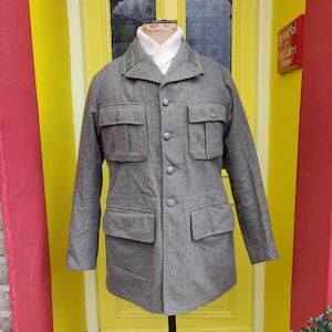 May include: A gray wool jacket with a button-up front and two large flap pockets. The jacket has a green and brown trim around the collar.