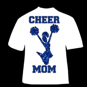May include: White t-shirt with the words "CHEER MOM" in blue glitter lettering. A blue glitter cheerleader silhouette is jumping with pom-poms. The shirt is a short-sleeved crew neck.