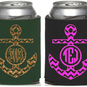 Op de afbeelding: Twee blikjeskoelers, &eacute;&eacute;n donkergroen met een gouden glitteranker en monogram, de andere zwart met een roze anker en monogram. Ontworpen om dranken koel te houden.