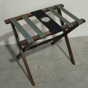 May include: A wooden luggage rack with a black canvas top and gray straps. The canvas top features a United States Navy seal.