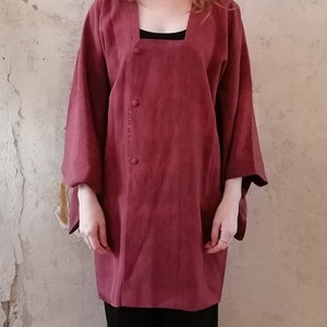 Op de afbeelding: Een lang, mouwloos jasje in kimono-stijl, bordeauxrood, met een vierkante halslijn en een enkele knoopsluiting. Het jasje heeft een textuur in de stof en is gemaakt van een lichtgewicht materiaal.