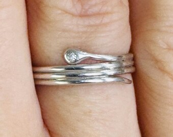 May include: A silver ring with a single small diamond set in the band. The ring is wrapped around the finger twice.