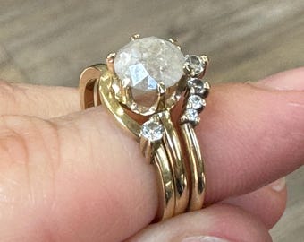 May include: A gold ring set with a large, round, clear, faceted gemstone surrounded by smaller clear gemstones. The ring is worn on a finger.