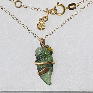 May include: A gold chain necklace with a green stone pendant wrapped in gold wire. The stone is a rough, natural shape.