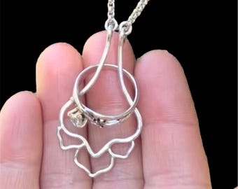 May include: A silver necklace with a ring holder pendant. The pendant is shaped like a flower with a small diamond in the center. The ring is held in place by the flower's petals.