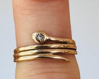 May include: A gold snake ring with a single diamond set in the head of the snake. The ring is wrapped around a finger.