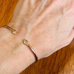 May include: A gold bangle bracelet with a simple design and rounded ends.