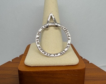 May include: A silver-colored pendant with a circular design and an upper-case letter "A" at the top. The circle has the engraved text "All my problems to Jesus". The pendant is displayed on a beige ring holder.