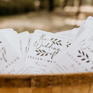 May include: A stack of white wedding ceremony programs with black calligraphy text. The top program features the text "The Wedding of Julian + MF/ The Ceremony" with a simple floral design.