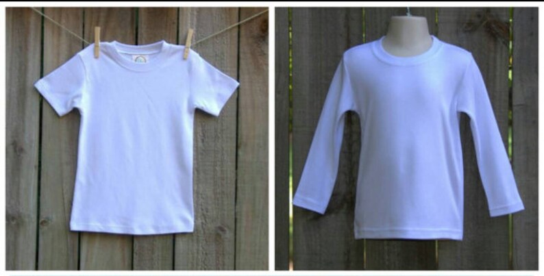 Op de afbeelding: Twee witte T-shirts, een met korte mouwen en een met lange mouwen, hangen aan een houten hek.