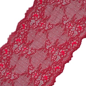 May include: A length of claret-coloured lace fabric with a scalloped edge. The lace features a floral pattern with small white dots and a delicate, open weave. The fabric is angled across a white background.