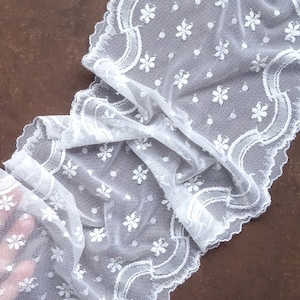 May include: White lace trim with a scalloped edge and a delicate floral pattern. The lace is sheer and has a soft, flowing texture.