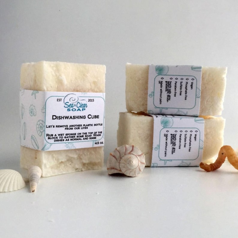 May include: Three white bars of dishwashing soap with a label that reads "Sea Clean Soap Dishwashing Cube 4.5 oz". The label also includes the text "Let's remove another plastic bottle from our lives. Rub a wet sponge on the top of the block to gather some soap. Wash dishes as normal and rinse."