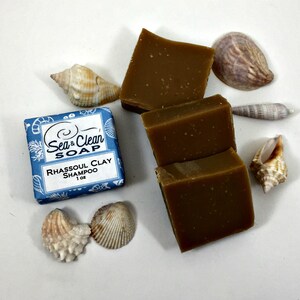 May include: Three bars of brown rhassoul clay shampoo soap, packaged in a blue box with the text "Sea & Clean Soap" and "Rhassoul Clay Shampoo 1 oz". The soap is surrounded by seashells.