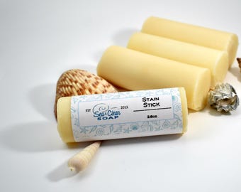 May include: A white bar of soap with a blue and white label that says "Sea Clean Soap" and "Stain Stick". The label also says "Est. 2015" and "2.6 oz". The soap is surrounded by seashells.