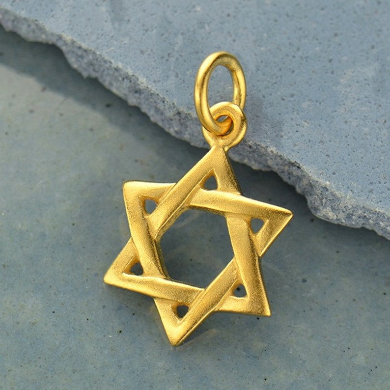 May include: A gold-colored pendant charm in the shape of a Star of David. The charm has a loop at the top for attaching to a necklace or bracelet.