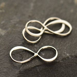 May include: Three silver infinity symbol charms, two stacked on top of each other, and one lying flat on a dark gray surface.