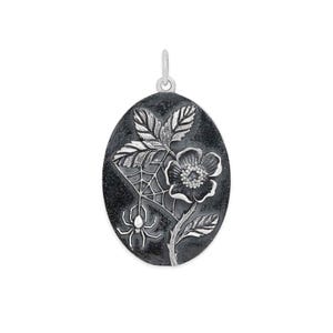 Op de afbeelding: Zilverkleurige ovale hanger met een bloemen- en spinnenwebontwerp. De hanger heeft een gedetailleerde bloem, bladeren en een spinnenweb met een spin. Het heeft een oogje om aan een ketting te bevestigen.