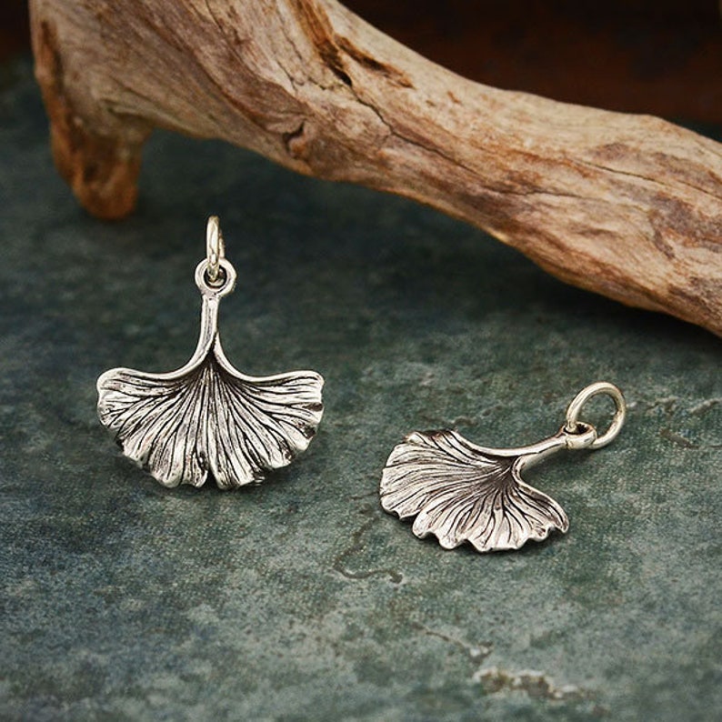 May include: Two silver ginkgo leaf charms with a detailed design. The charms are perfect for jewelry making or crafting.