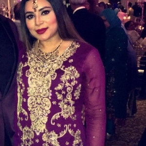 Puede incluir: Una mujer con un vestido bordado en morado y dorado con pantalones dorados y zapatos plateados. Est&aacute; de pie en una habitaci&oacute;n con suelo de madera.