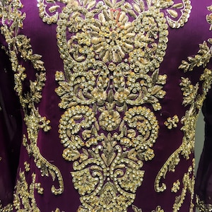 Puede incluir: Una prenda de vestir morada con intrincados bordados dorados y adornos. El dise&ntilde;o presenta un motivo floral con brillantes pedrer&iacute;a.