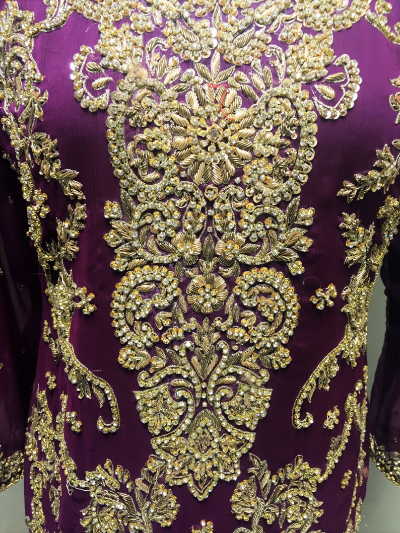 Puede incluir: Una prenda de vestir morada con intrincados bordados dorados y adornos. El dise&ntilde;o presenta un motivo floral con brillantes pedrer&iacute;a.