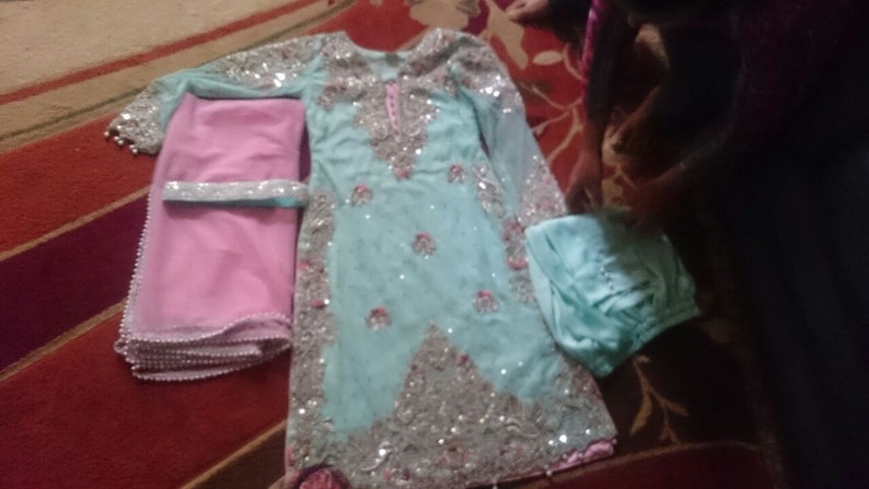May include: A light blue and pink outfit with silver embellishments. The outfit includes a long-sleeved top, a pair of trousers, and a dupatta.