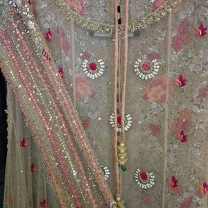 May include: A beige net fabric garment with pink and gold embroidery. The garment has a round neckline and a long, flowing design. The fabric is embellished with sequins and beads.