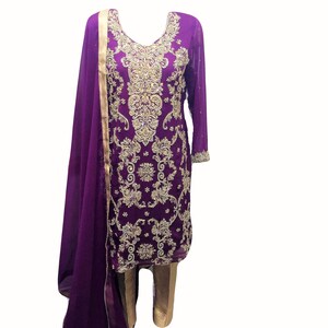 Puede incluir: Un vestido bordado en morado y dorado con un dupatta a juego. El vestido tiene un escote en V y mangas largas. El dupatta es una larga bufanda fluida que a menudo se usa con ropa india.