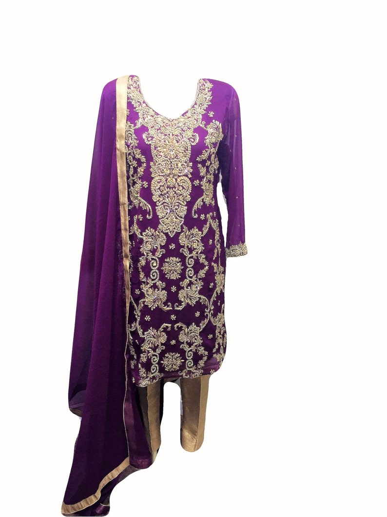 Puede incluir: Un vestido bordado en morado y dorado con un dupatta a juego. El vestido tiene un escote en V y mangas largas. El dupatta es una larga bufanda fluida que a menudo se usa con ropa india.