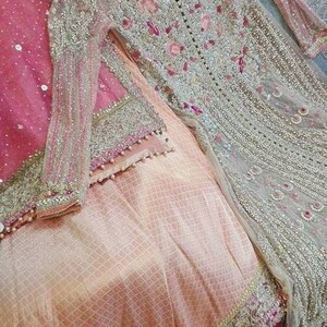 May include: A light pink and silver embroidered dress with a sheer overlay and a matching dupatta. The dress has a beaded trim and floral embroidery.