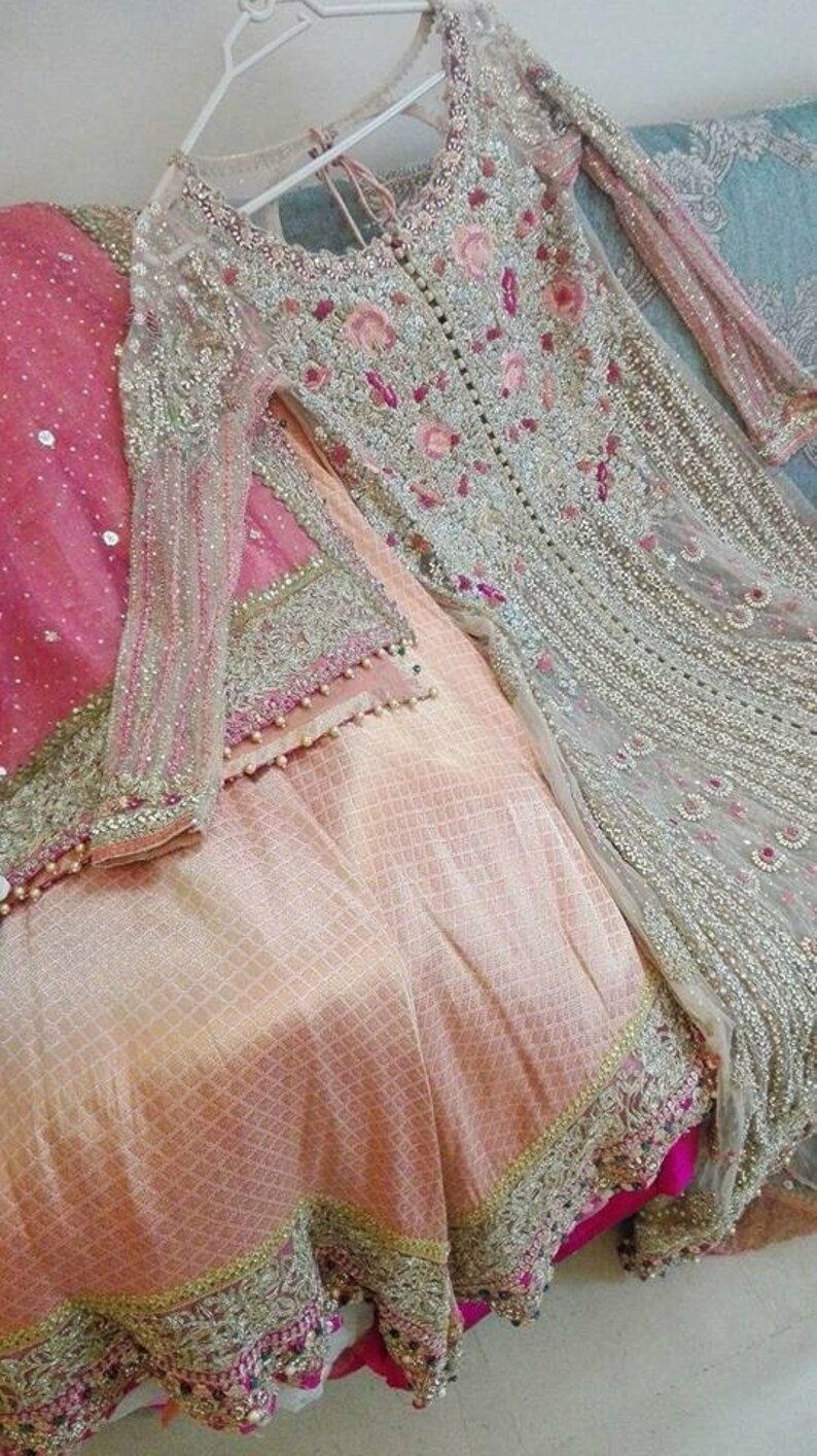 May include: A light pink and silver embroidered dress with a sheer overlay and a matching dupatta. The dress has a beaded trim and floral embroidery.