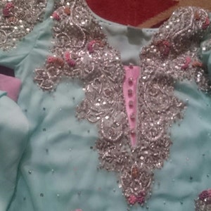 May include: A light blue dress with silver and pink embellishments. The dress has a long sleeve and a high neckline.