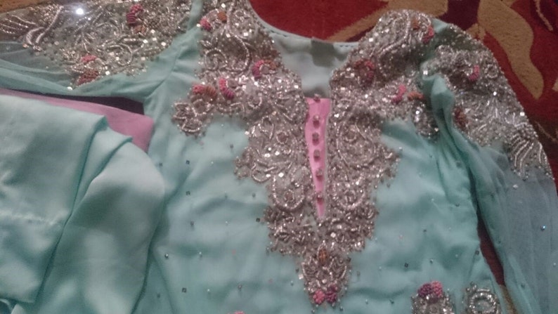 May include: A light blue dress with silver and pink embellishments. The dress has a long sleeve and a high neckline.