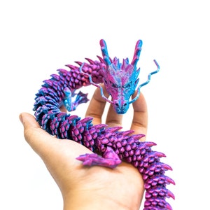 May include: A purple and blue dragon figurine with a curled tail, held in someone's hand.