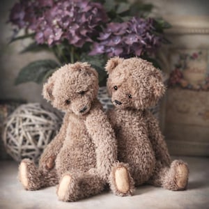 Peut inclure: Deux ours en peluche bruns avec une fourrure touffue sont assis côte à côte. Ils ont de petits yeux noirs et des coussinets de pattes beiges. Un vase de fleurs violettes et une boule décorative sont en arrière-plan.