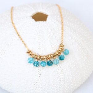 Puede incluir: Un collar de cadena dorada con un racimo de cuentas de piedras preciosas azul verdosas que cuelgan del centro.