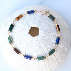 Può includere: Un braccialetto d'oro con perline di lapislazzuli blu, giada verde e occhio di tigre.