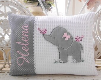 Puede incluir: Una almohada gris y blanca con un elefante gris y dos pájaros rosas bordados. La almohada tiene un lado gris con lunares blancos y el nombre "Helena" bordado en rosa.