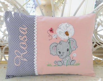 Puede incluir: Un cojín decorativo con un estampado de lunares grises en el lado izquierdo y un fondo rosa en el lado derecho. El nombre "Rosa" está bordado en rosa. Un elefante bordado sostiene un diente de león.