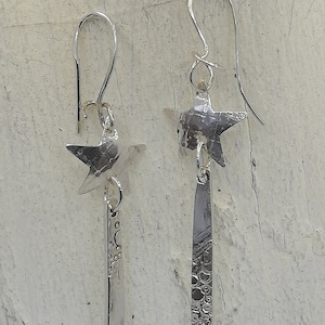Peut inclure: Une paire de boucles d'oreilles pendantes en argent avec un charme en forme d'étoile et un pendentif en forme de barre texturée.