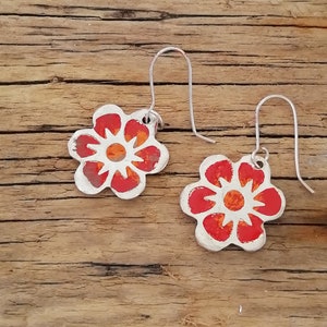 May include: A pair of silver earrings with red and orange flower designs. The flowers have white centers and are painted with a textured finish.