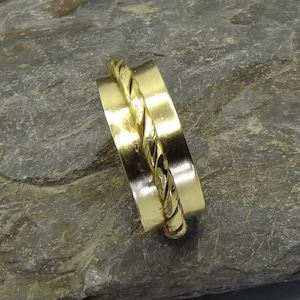 Puede incluir: Un anillo de oro con un diseño trenzado. El anillo está hecho de dos bandas, una con un acabado liso y la otra con un patrón trenzado.
