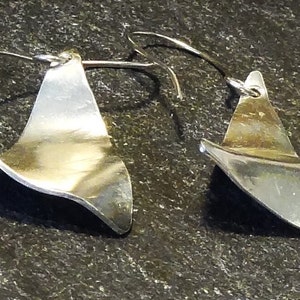 May include: A pair of silver earrings with a unique, wavy, asymmetrical design. The earrings are made of a smooth, polished metal and have a modern, minimalist aesthetic.